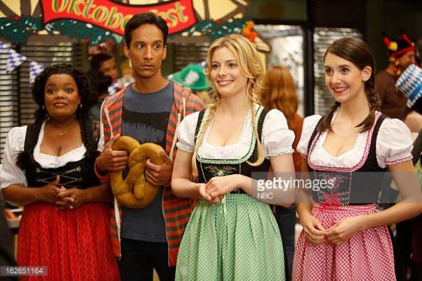 trois femmes de couleurs distinctes habillées d'habit traditionnels allemands jouent les poticles avec au milieu un grand homme de couleur à l'air nigaud qui tient un bretzel